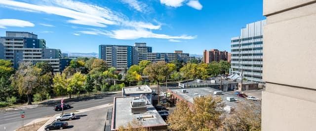 Urban apartment view overlooking street, parking lot, trees, and multi-story residential buildings under blue sky